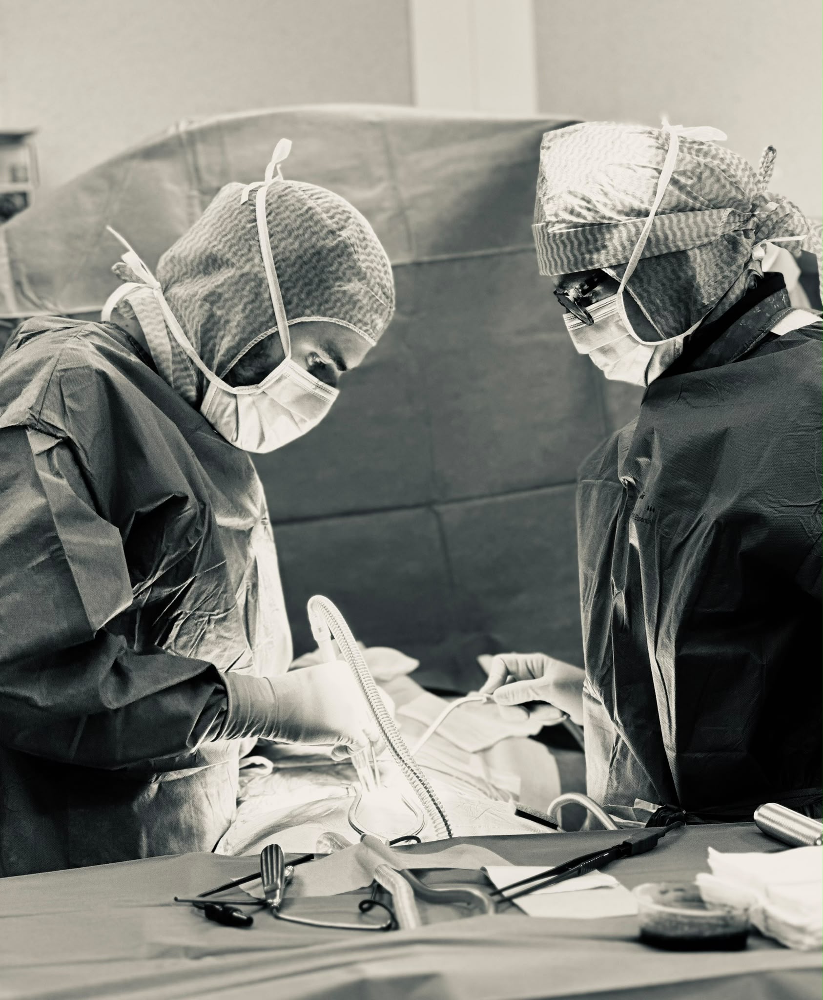 Deux soignants en tenue stérile penchés au-dessus du patient au bloc opératoire — attention constante et gestes précis